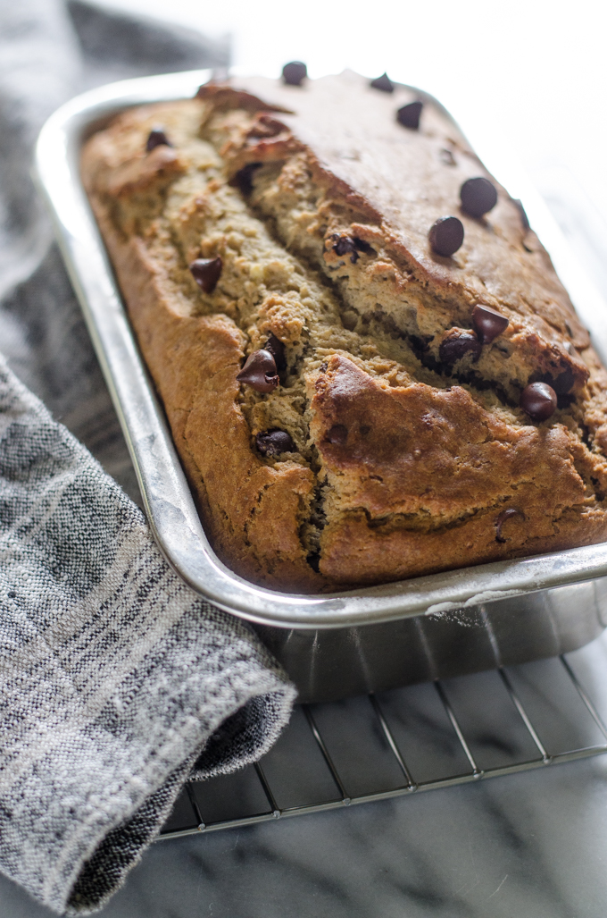 Sourdough banana bread in loaf pan on a cooling rack on a marble surface.