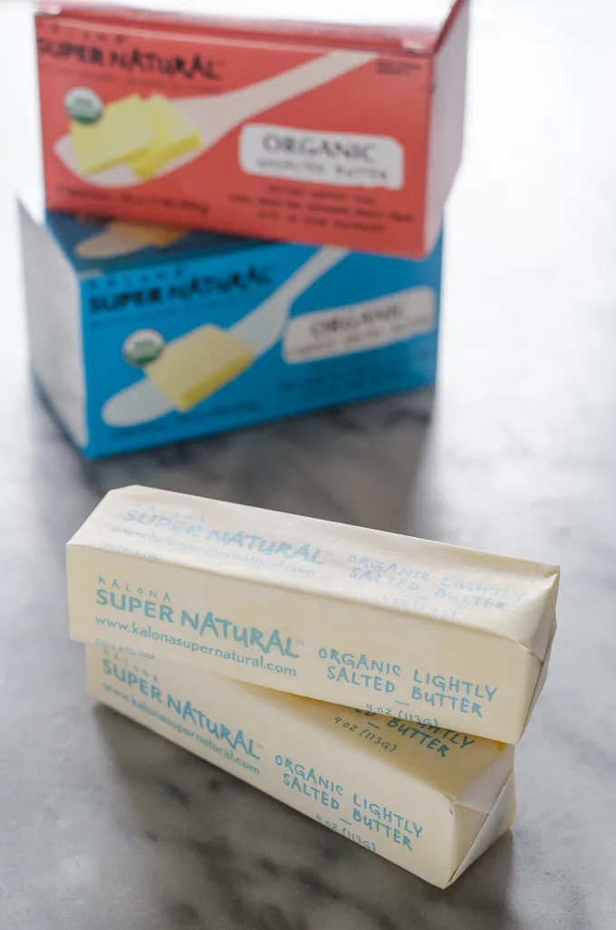 Sticks of Kalona SuperNatural butter on a marble surface with packaging in the background.