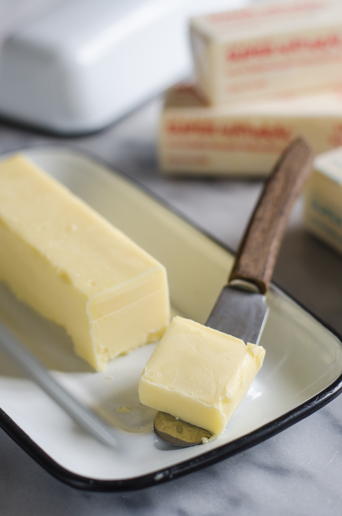 Butter in an enamel butter dish with a slice on a butter knife.