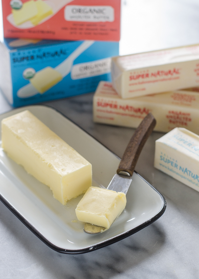 Butter in an enamel butter dish with a slice on a butter knife.