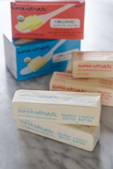 Sticks of Kalona SuperNatural butter on a marble surface with packaging in the background.