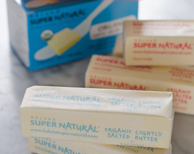 Sticks of Kalona SuperNatural butter on a marble surface with packaging in the background.