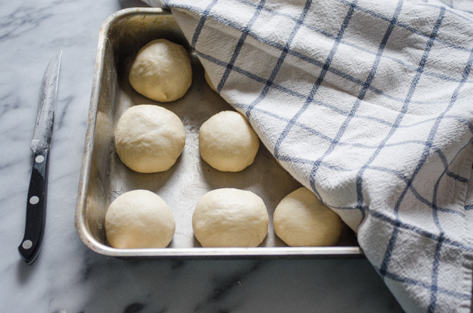 The balls of dough in a 13x9 inch stainless steel pan with a checkered tea towel draped over them.