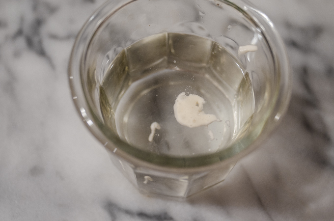 A small piece of sourdough starter floating in a glass of water.