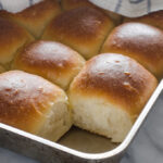 Pan of sourdough pull apart rolls with one taken out of the pan.