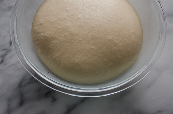 The risen dough in a glass bowl.