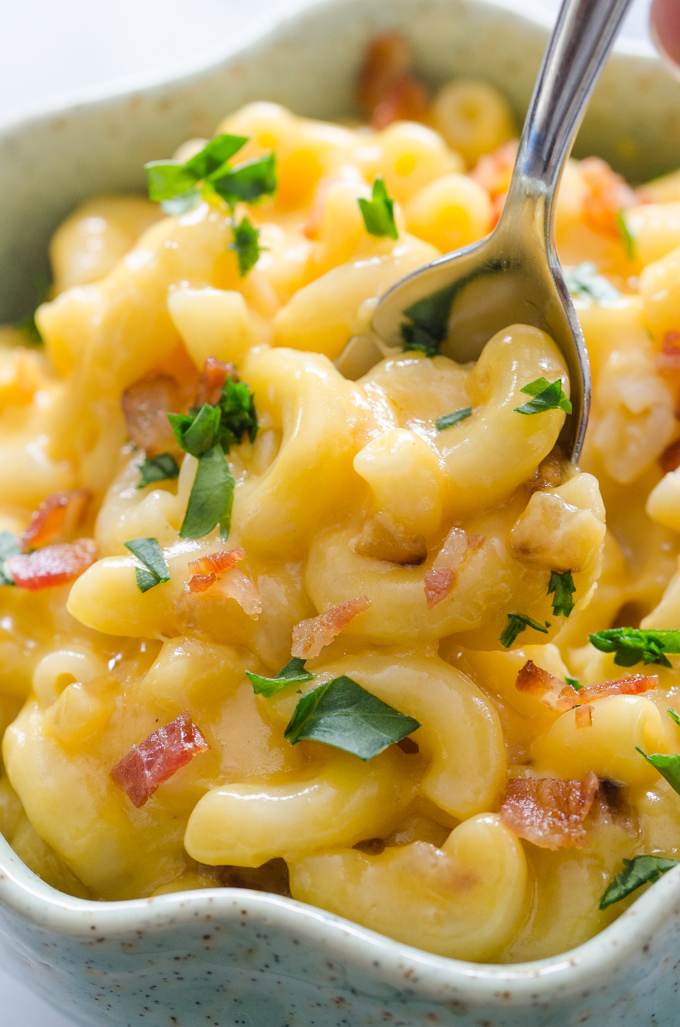 A closeup shot of a bowl of butternut squash mac and cheese garnished with parsley and bacon.