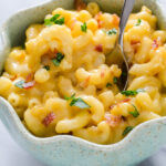 A closeup shot of a bowl of butternut squash mac and cheese garnished with parsley and bacon.