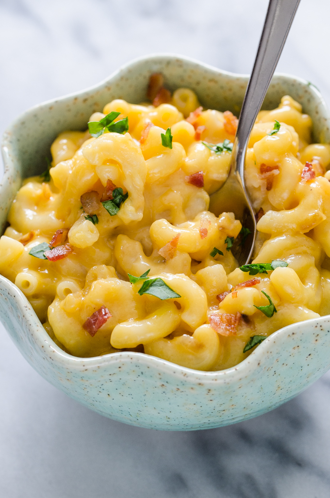 A closeup shot of a bowl of butternut squash mac and cheese garnished with parsley and bacon.