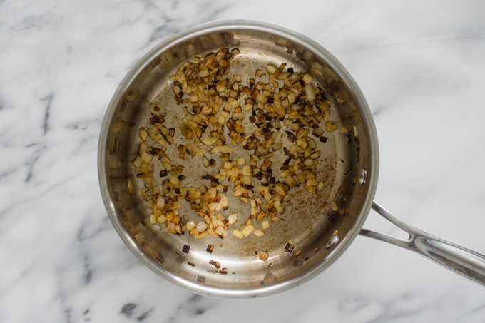 Fried onions in a stainless steel pan on a marble surface.