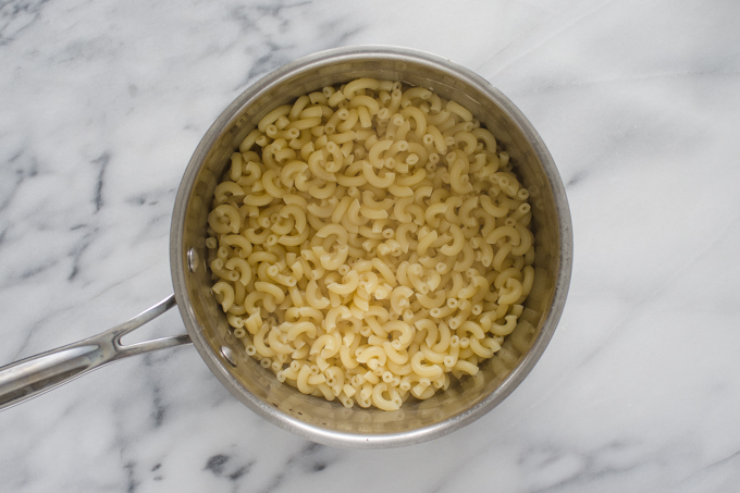Cooked macaroni noodles in a stainless steel pot on a marble surface.