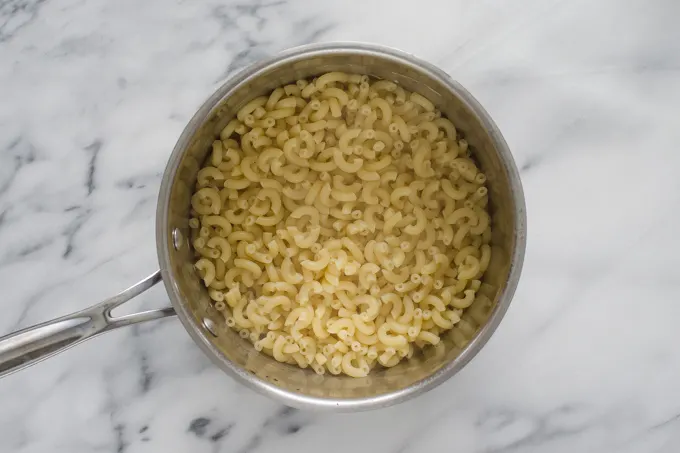 Cooked macaroni noodles in a stainless steel pot on a marble surface.