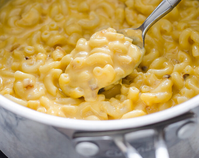 A spoonful of butternut squash mac and cheese held over the pot.