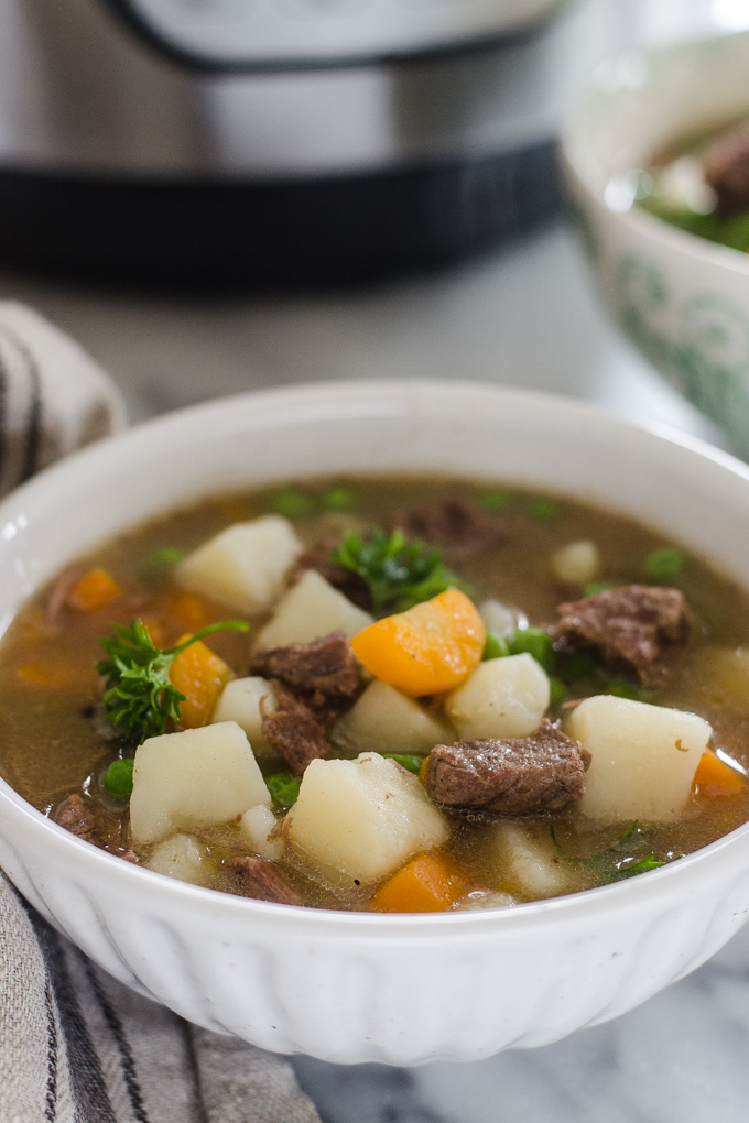 Bowls of Instant Pot Beef Stew with the pressure cooker in the background.