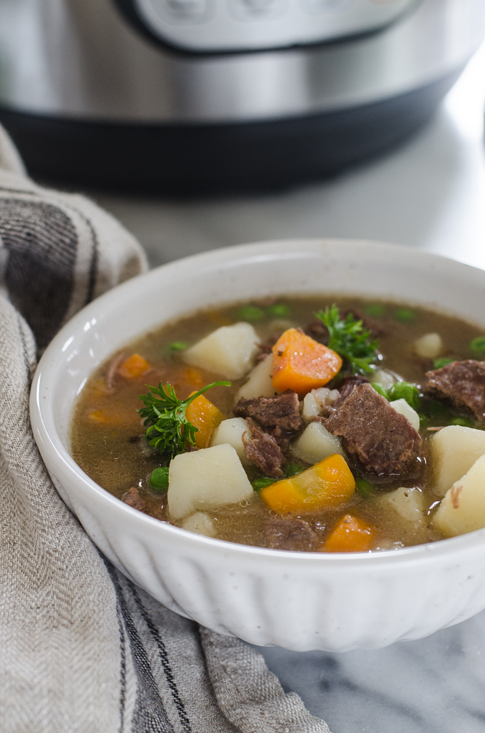 A bowl of Instant Pot Beef Stew with the pressure cooker in the background.