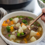 A bowl of Instant Pot Beef Stew with the pressure cooker in the background.