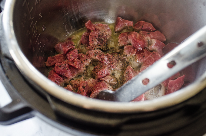 Adding salt and pepper to the beef in the Instant Pot.