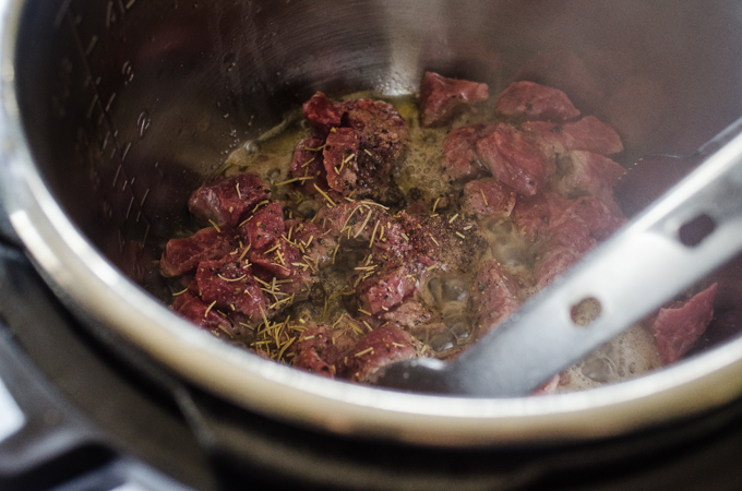 Adding rosemary to the beef in the Instant Pot.