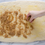 Sprinkling the cinnamon sugar mixture on top of the butter on the dough.