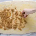 Sprinkling the cinnamon sugar mixture on top of the butter on the dough.