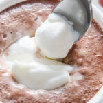 Spooning whipped cream into a mug of cocoa.