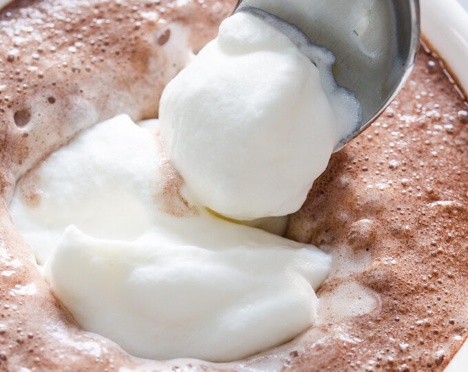 Spooning whipped cream into a mug of cocoa.