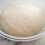 The risen sourdough french bread dough in a large bowl on a marble surface.