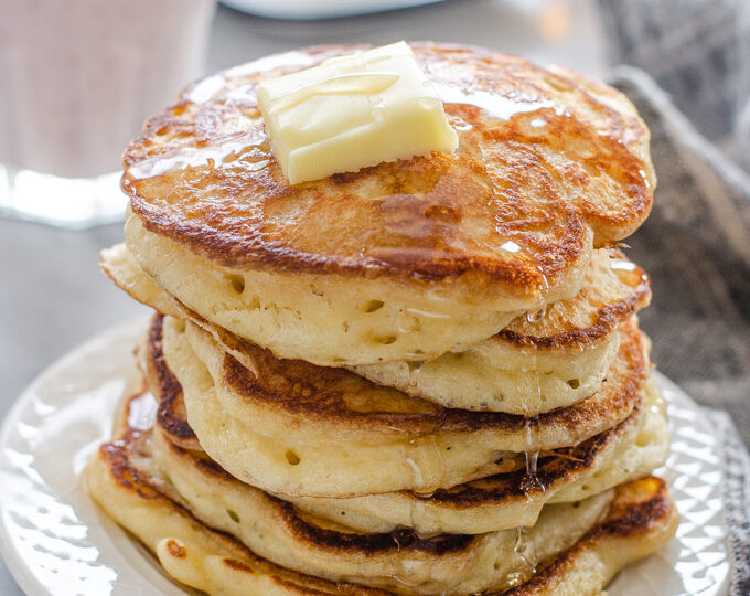 A stack of sourdough pancakes with a pat of butter and maple syrup dripping off the sides.