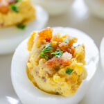 Close up shot of deviled eggs with bacon and parsley.