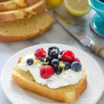 A slice of sour cream pound cake loaf topped with whipped cream and berries.