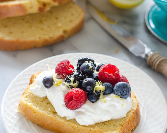 A slice of sour cream pound cake loaf topped with whipped cream and berries.