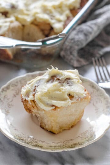 A sourdough cinnamon roll with cream cheese icing on a small plate.