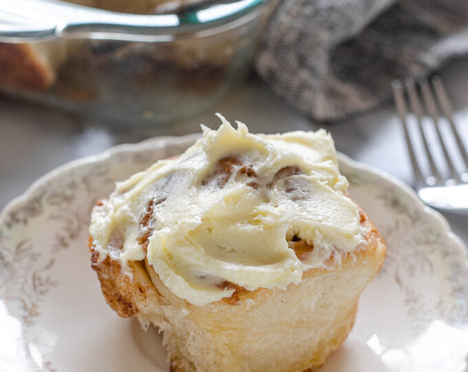 A sourdough cinnamon roll with cream cheese icing on a small plate.