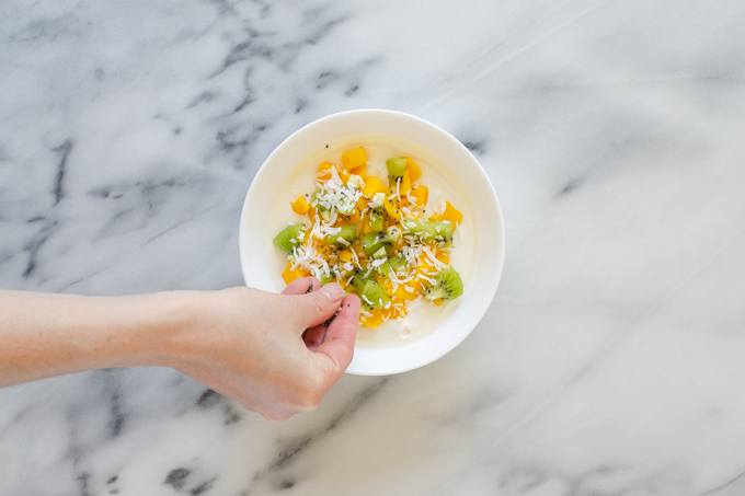 Adding mangoes, kiwi, coconut, and chia seeds to the yogurt.