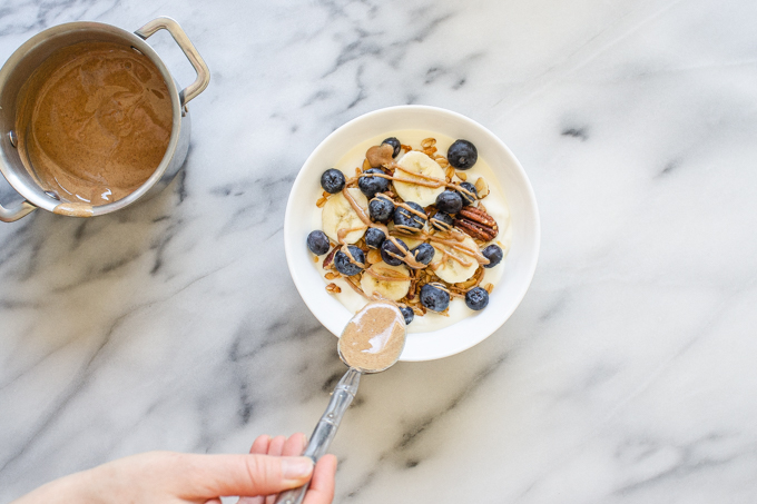 Drizzling almond butter over the yogurt, bananas, blueberries, and granola.