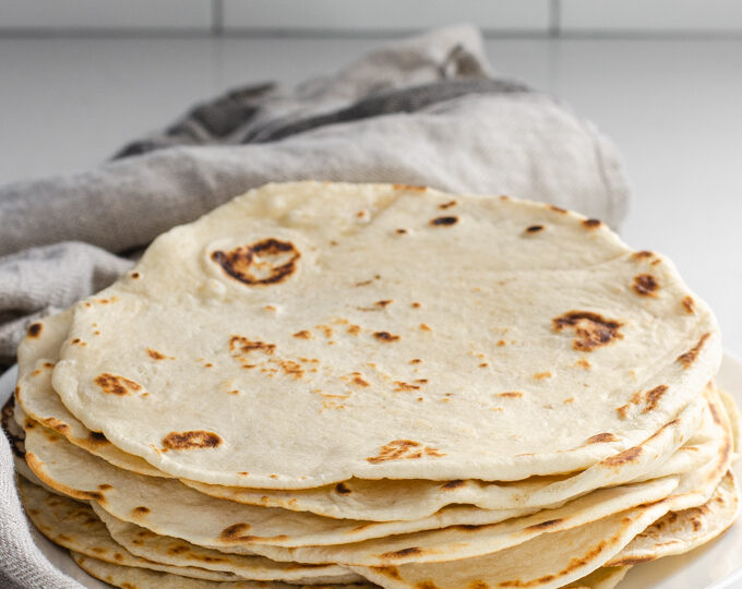 Sourdough tortillas stacked on a plate with a tea towel around them.