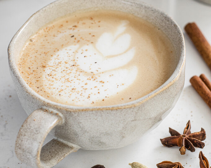 A mug of dirty chai latte with spices around it.