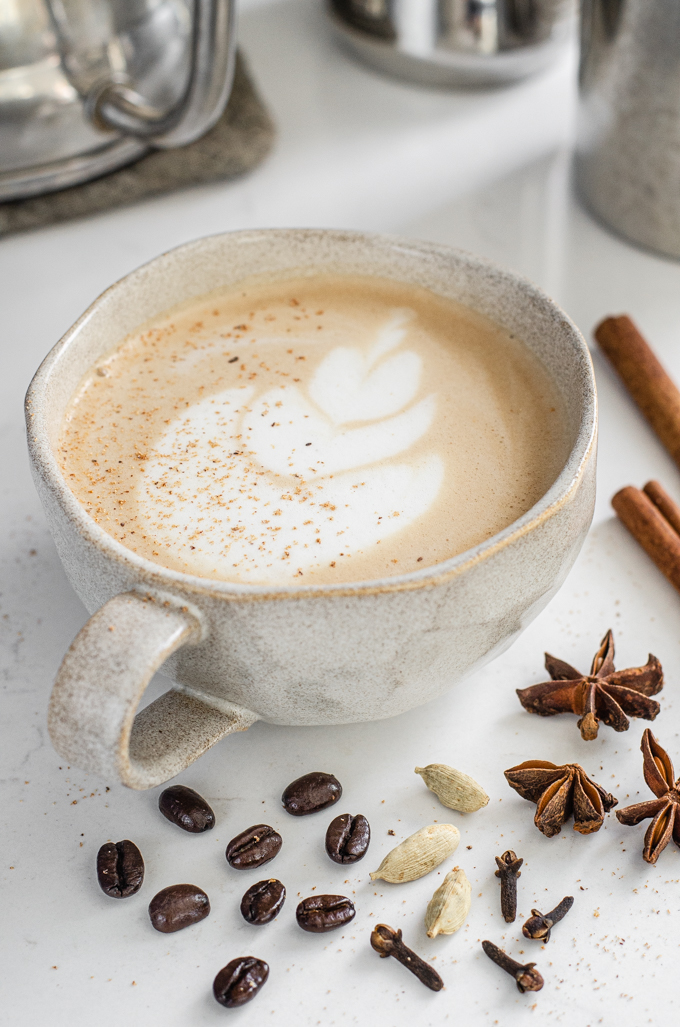 A mug of dirty chai latte with spices around it.