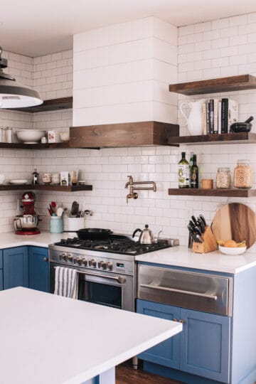 Transitional industrial farmhouse style kitchen with blue cabinets, subway tile backsplash, white quartz counters, and open shelving.