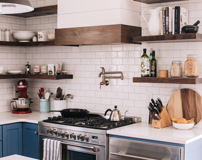 Transitional industrial farmhouse style kitchen with blue cabinets, subway tile backsplash, white quartz counters, and open shelving.