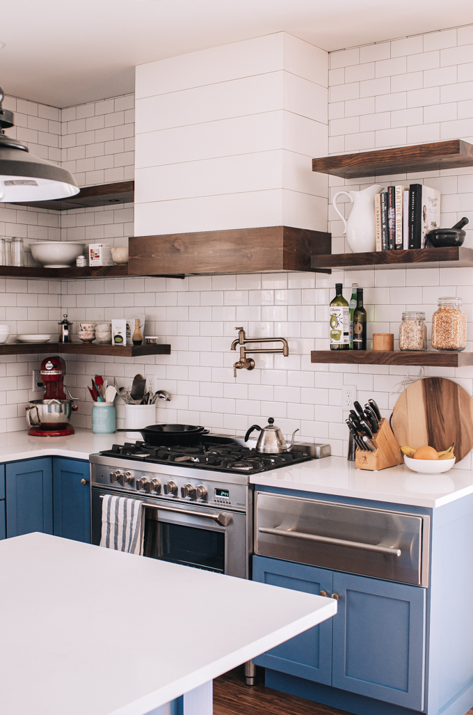 Transitional industrial farmhouse style kitchen with blue cabinets, subway tile backsplash, white quartz counters, and open shelving.