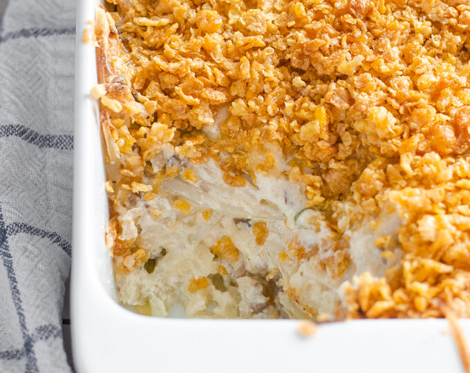 The baked gluten free cheesy potatoes (AKA funeral potatoes) in a white casserole dish on top of a wire cooling rack with a scoop taken out.