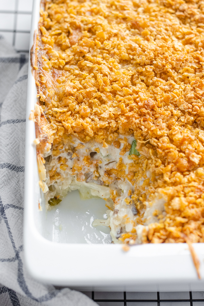 The baked gluten free cheesy potatoes (AKA funeral potatoes) in a white casserole dish on top of a wire cooling rack with a scoop taken out.