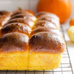 Pumpkin sourdough dinner rolls on a black wire cooling rack.