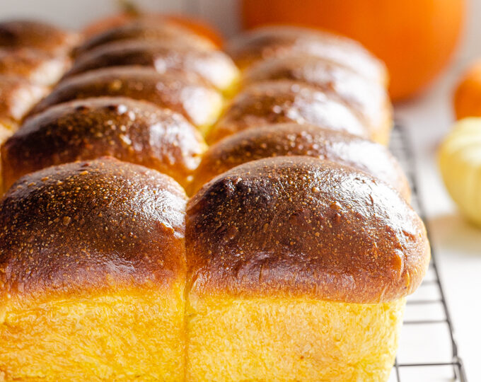 Pumpkin sourdough dinner rolls on a black wire cooling rack.