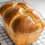 A loaf of sourdough brioche bread on a black wire cooling rack.