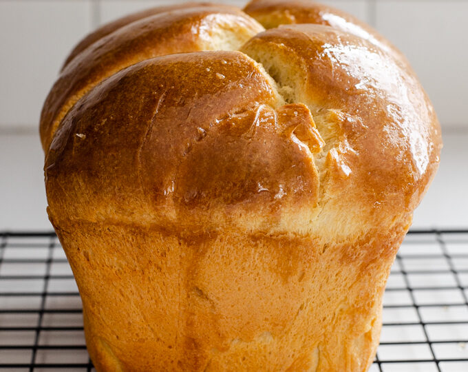 A loaf of sourdough brioche bread on a black wire cooling rack.