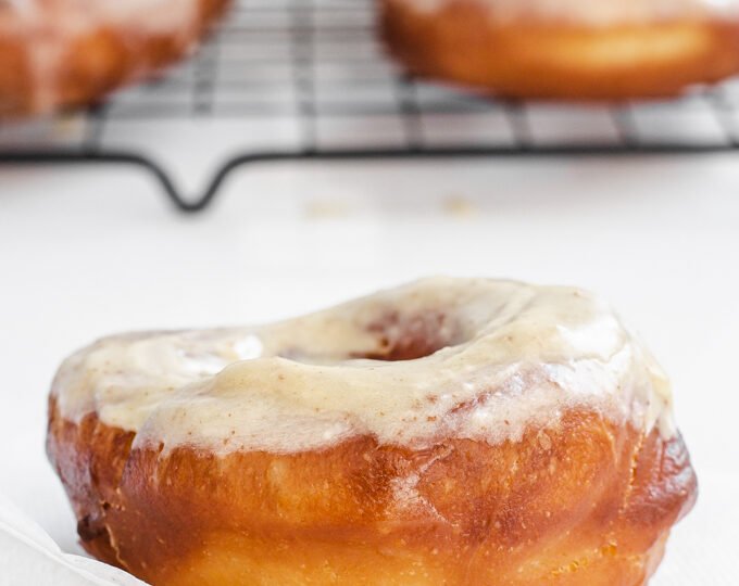 A donut on a napkin with more sourdough donuts on a wire cooling rack in the background.