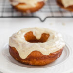 A sourdough donut on a plate with more doughnuts behind it on a wire cooling rack.