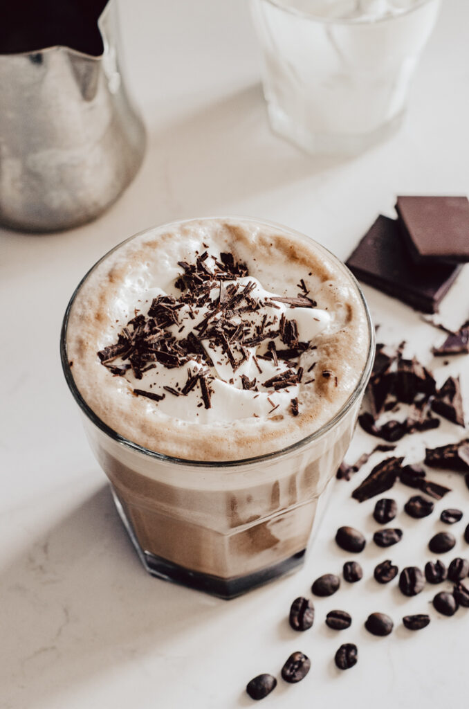 A glass filled with a mocha latte with coffee beans and chocolate off to the side.